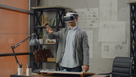 Male-engineer-in-the-office-in-a-virtual-reality-helmet-uses-gestures-to-manage-the-project-without-leaving-the-office.-Construction-control.-Design-project-of-the-building-and-interior